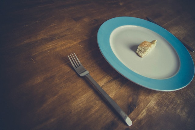 Kúsok bieleho chleba na tanieri a vidlička na drevenom stole.jpg